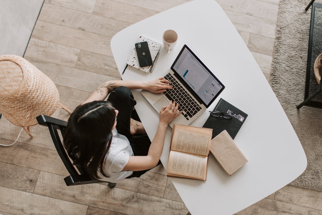 junge dunkelhaarige Frau mit Notebook und Büchern am privaten Arbeitsplatz, senkrecht von oben aufgenommen